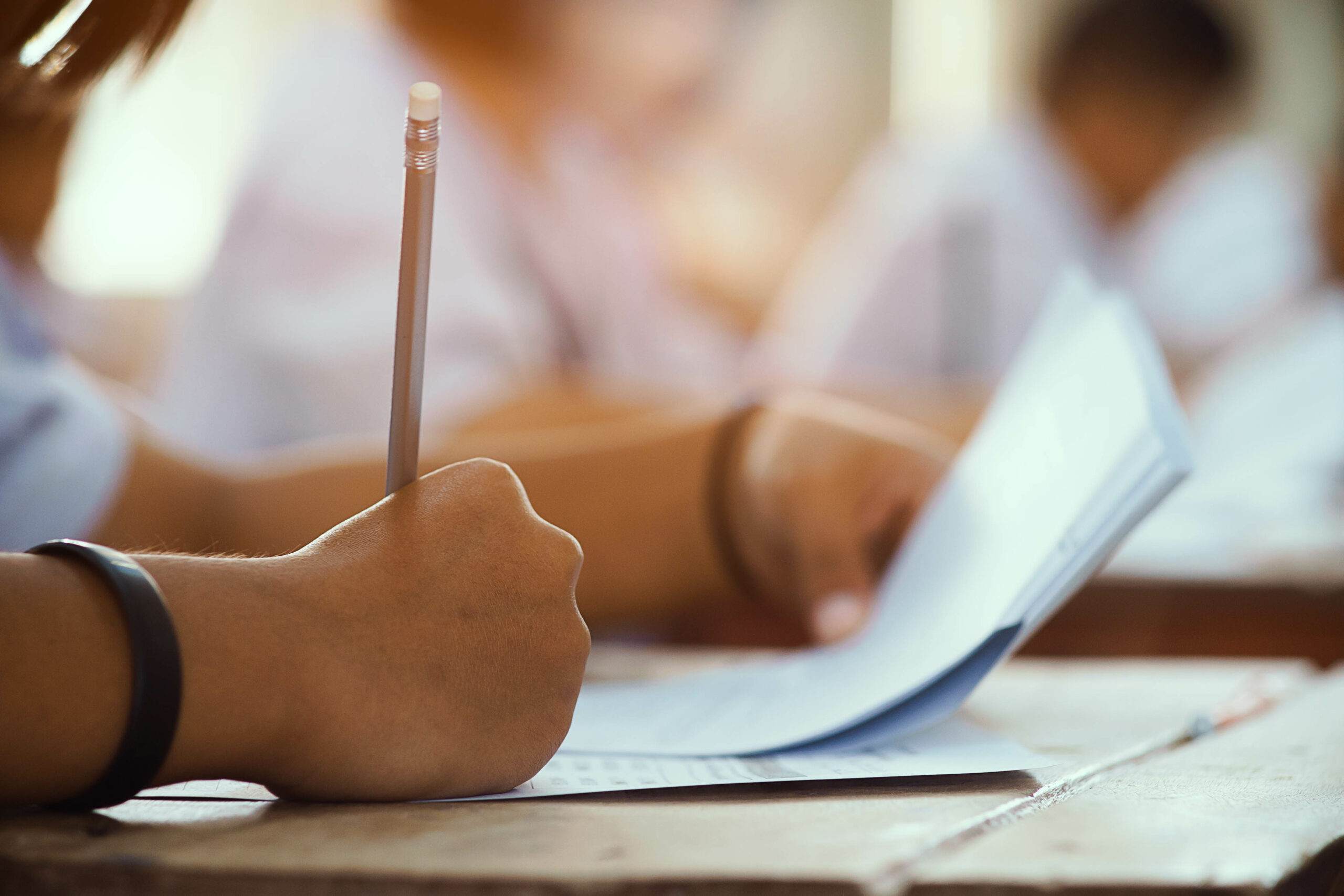 Closeup to hand of student  holding pencil and taking exam in classroom with stress for education test.