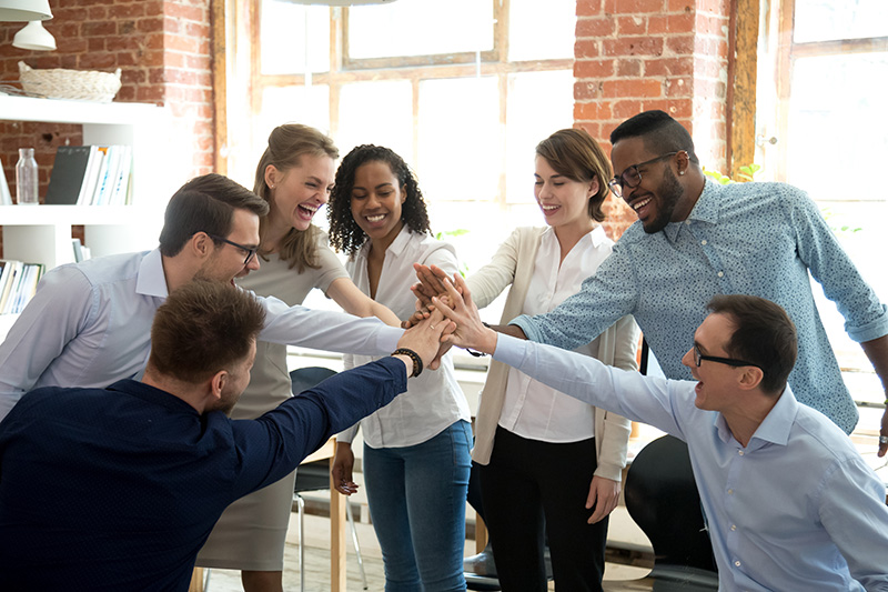 Excited multiracial colleagues give high five involved in teambuilding activity at meeting, happy diverse workers join hands celebrate success or win, show team spirit and unity. Cooperation concept