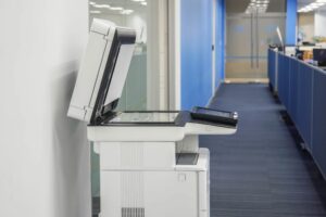 A standalone all in one printer with an open scanner lid positioned in the hallway of an office, illustrating a common scene in a corporate environment where multifunctional printing devices are essential.