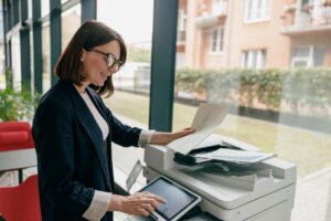Smiling businesswoman using an all in one office printer to scan or copy documents in a bright office setting.