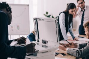 Business professionals work in a bright, modern office where one works in the foreground making copies on an office copier.
