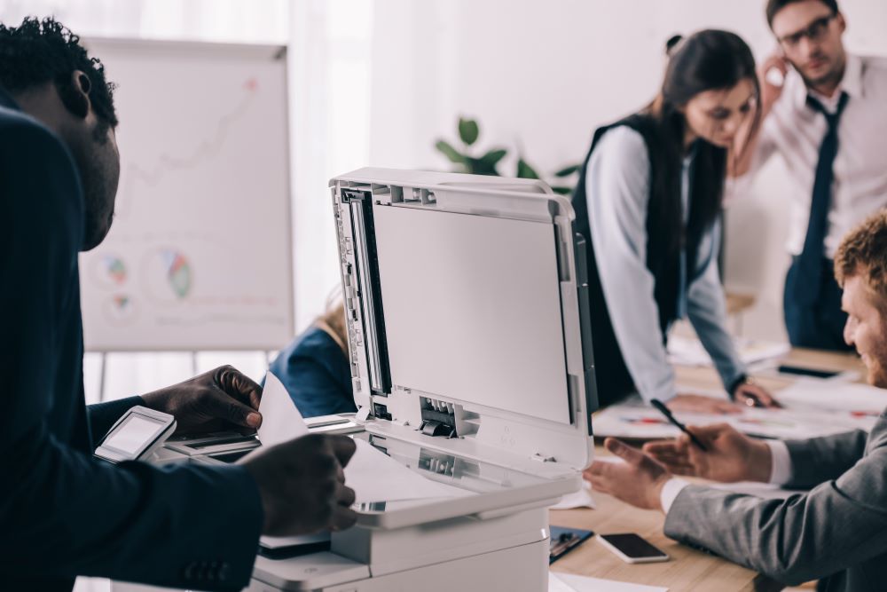 Business professionals work in a bright, modern office where one works in the foreground making copies on an office copier.